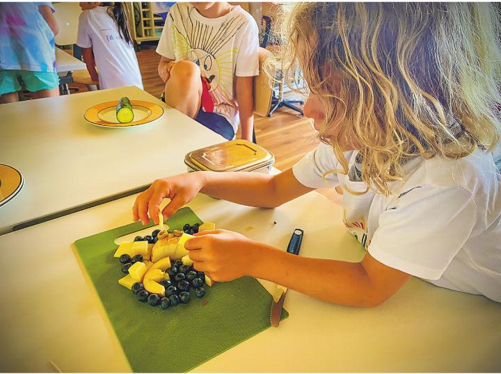 Konzentriert werden Heidelbeeren, Apfelschnitze und eine Olive zu einer kunstvollen Krabbe arrangiert.
